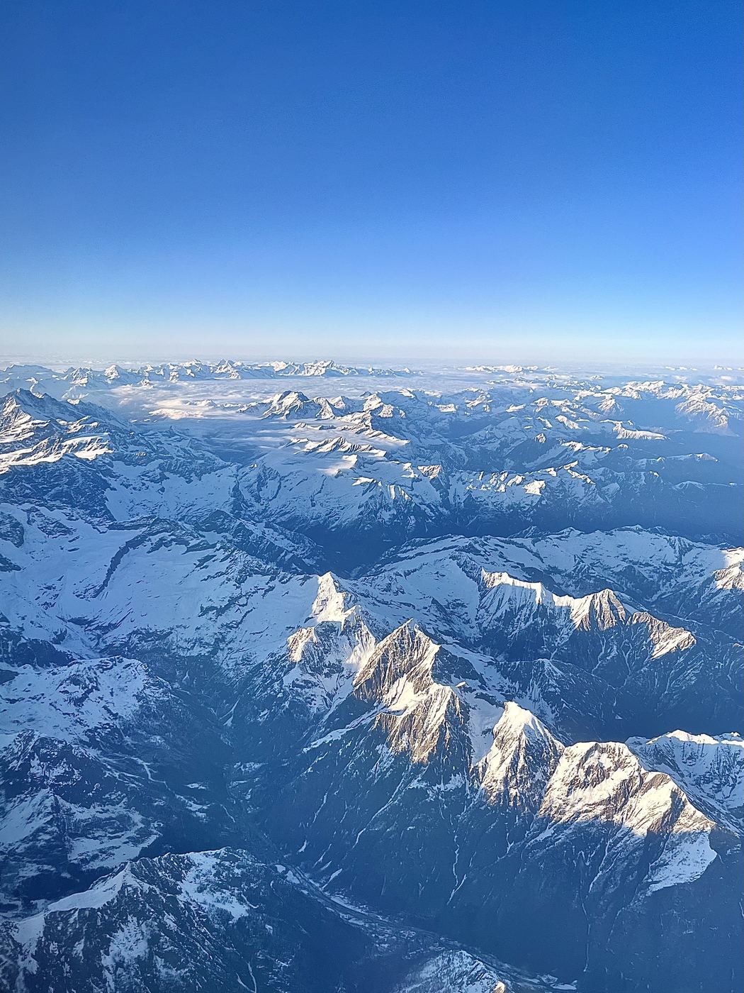 The Alps from the air, snow-covered peaks under a clear sky.
