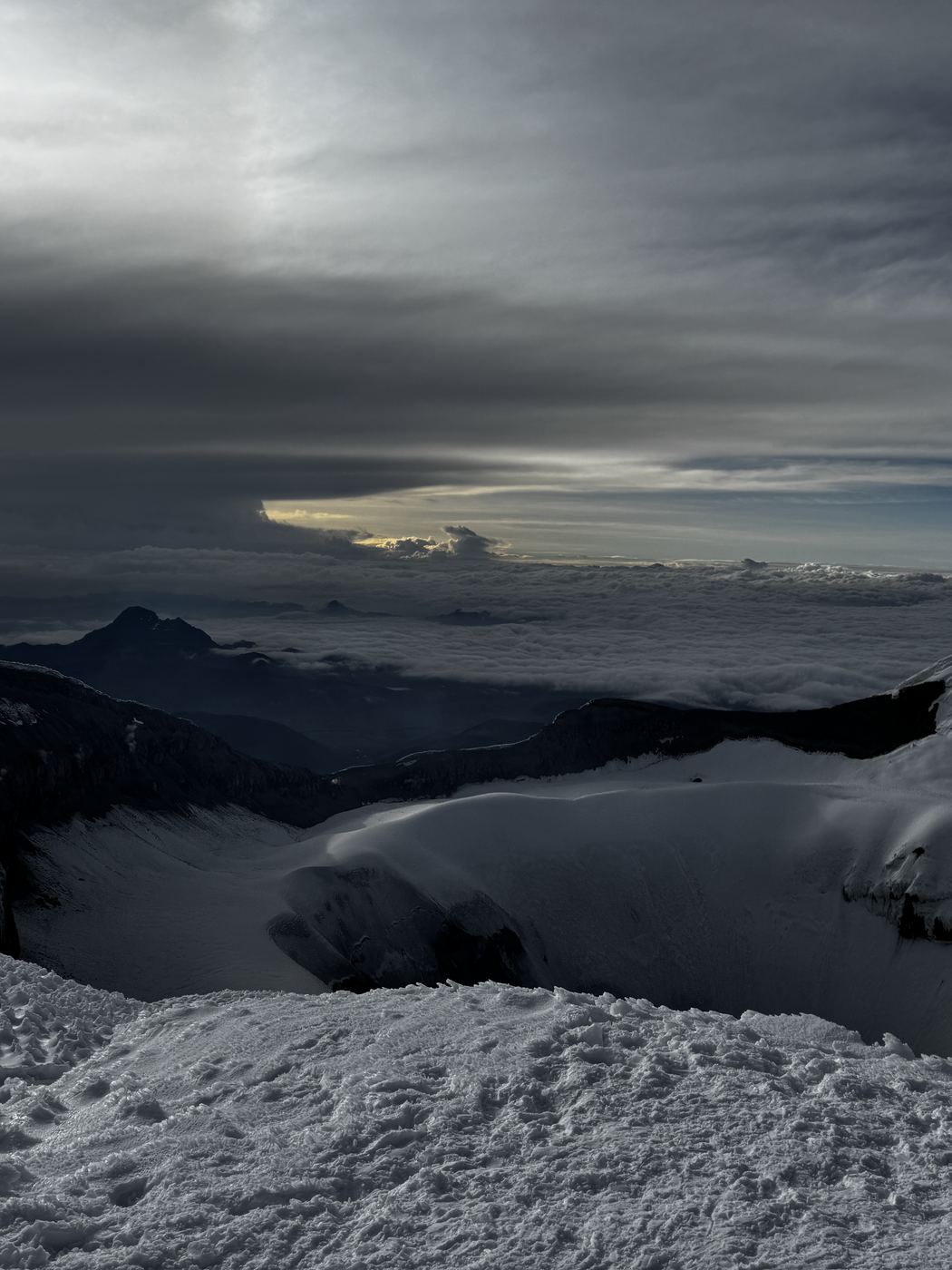 A dark cloud layer below the Cotopaxi glacier, a distant peak on the horizon.