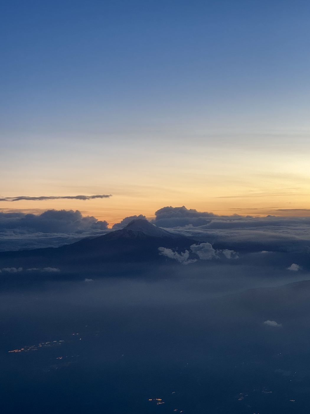 Sunrise above the clouds, a volcano silhouetted on the horizon.